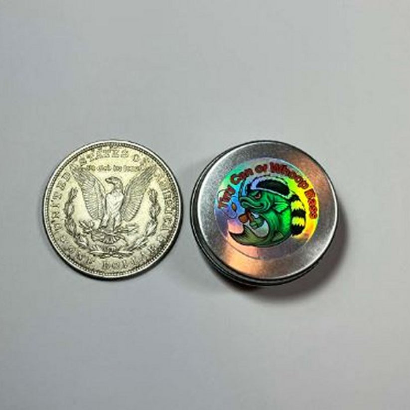 Small fishing‑kit can with new logo placed next to a dollar coin to illustrate size